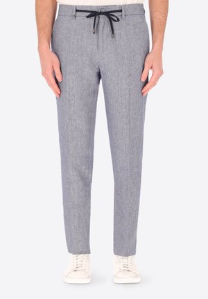 Pantaloni slim fit grigio chiaro con trama e coulisse nera, indossati con scarpe da ginnastica bianche e camicia bianca infilata.