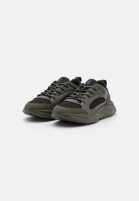 Scarpe sportive caratterizzate da una combinazione di rete e materiali in gomma di colore verde scuro e nero, con una forma arrotondata e una suola testurizzata.