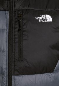 Černá a šedá zateplená bunda s kapsou na zip a bílým logem "The North Face". Hladký povrch a nadýchaný design.