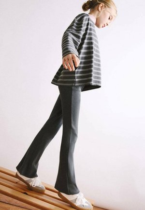 Haut à manches longues rayé gris, coupe décontractée ; associé à un pantalon évasé gris foncé. Chaussures avec semelles claires et lacets blancs.