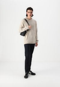 Kremasta pletiva veste s teksturiranim tkanjem, crna torba preko ramena, tamne hlače i crne tenisice s bijelim detaljima. Jednostavna, minimalistička odjeća.