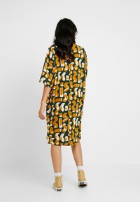 Přesně padnoucí šaty s krátkým rukávem v zelené barvě s abstraktními vzory v hořčicové a bílé, s volným střihem a střední délky.