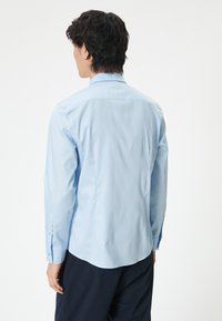 Ljusblå långärmad skjorta i mjukt tyg. Har en spetsig krage, rundad nederkant och knappade ärmslut. Enkelt design, utan mönster.