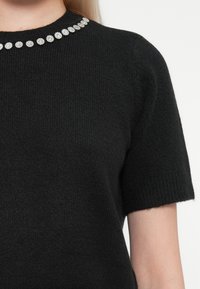 Black knitted sweater with short sleeves, featuring a round neckline adorned with clear rhinestones around the collar.