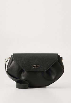Black Guess leather half-moon crossbody bag with a flap closure, gold logo, and adjustable shoulder strap on a white background.