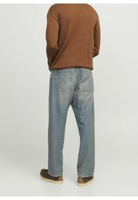 Hellblaue Jeans aus Denim mit lockerem Sitz, ausgestattet mit Gesäßtaschen und sichtbaren Nähten, kombiniert mit einem braunen, strukturierten Pullover und braunen Schuhen.