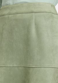 Gros plan d'une jupe en daim vert clair montrant la ceinture et les coutures détaillées.