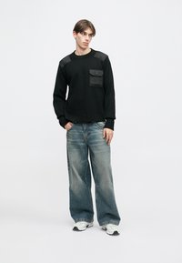 Hanorac negru cu accente pe umeri și buzunar frontal, asortat cu blugi largi, albastru deschis, și adidași albi. Design simplu, casual.