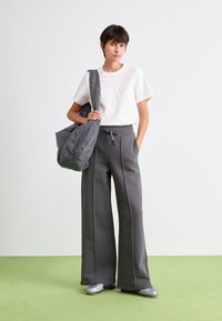 Grå vidde sweatpants med sidesømme, parret med en hvid t-shirt med korte ærmer. En tekstureret grå taske slænget over skulderen. Sølvfargede sko.