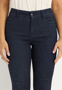 Mörkblå högmidjade jeans i denim, med dragkedja och knappknäppning, fem fickor och en jämn yta.