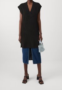 Abito smanicato nero in maglia con scollo a V, abbinato a una gonna di jeans con uno spacco frontale e una piccola borsa blu. Sandali neri chunky.