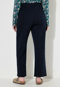 Tummansiniset housut, joissa on huomaamaton lehtikuvio, suoralinjainen malli ja korkea vyötärö, yhdistettynä vaaleisiin puukenkään.