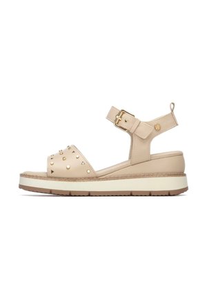 Sandalias beige con correa en el tobillo, hebilla dorada, parte superior texturizada, detalles con tachuelas y suela plataforma con una franja blanca contrastante.