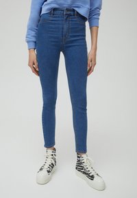 Vysoké skinny džíny v tmavě modrém denimu s hladkou texturou. Spárované s černobílými vzorovanými vysokými teniskami.