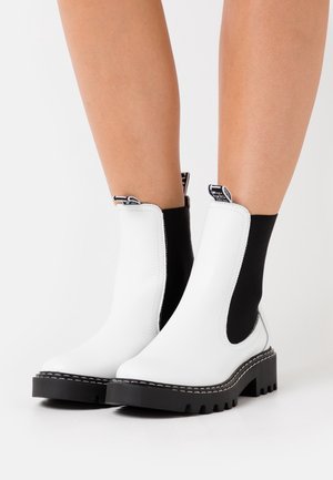 Botas de tobillo de cuero blanco con paneles laterales elásticos negros, suelas de goma negra gruesa y detalle de costura en contraste. Adecuadas para un uso casual.