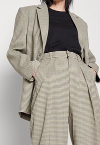 Svetle zelený kostkovaný blazer s přezvětšenými rameny, v kombinaci s černým přiléhavým topem a vysokými skládacími kalhotami s kostkovaným vzorem.