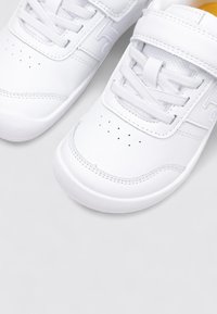 Zapatillas blancas con parte superior de cuero texturizado, cierres de cordones y velcro, puntera redondeada y perforaciones en la caja de los dedos para mayor transpirabilidad.