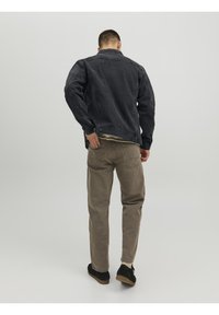 Black denim jacket, relaxed fit, button closure, paired with light brown cotton pants, textured fabric, black suede shoes with gum sole.