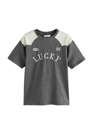 T-shirt en coton gris avec des épaules crème, affiche "LUCKY 89" en texte blanc. Manches courtes, tissu légèrement texturé, coupe décontractée.
