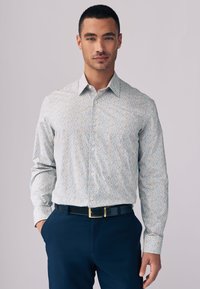 Skjorte med knapper i lyseblå med et spredt blomsterprint i gult og blåt. Lange ærmer, krave og kombineret med mørke bukser.