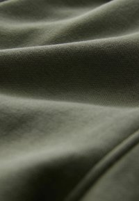 Olivgrüner Baumwollstoff mit glatter Textur, der subtile Falten und Furchen aufweist und die Flexibilität und den Fall des Materials einfängt.
