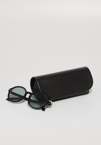 Black round sunglasses with dark lenses and gold accents, positioned next to a black leather case. The case has a smooth texture.