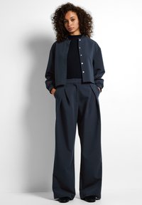 Chaqueta corta de un oscuro azul marino con cierre de botones plateados, combinada con pantalones de pierna ancha y a cintura alta en tela y color a juego.