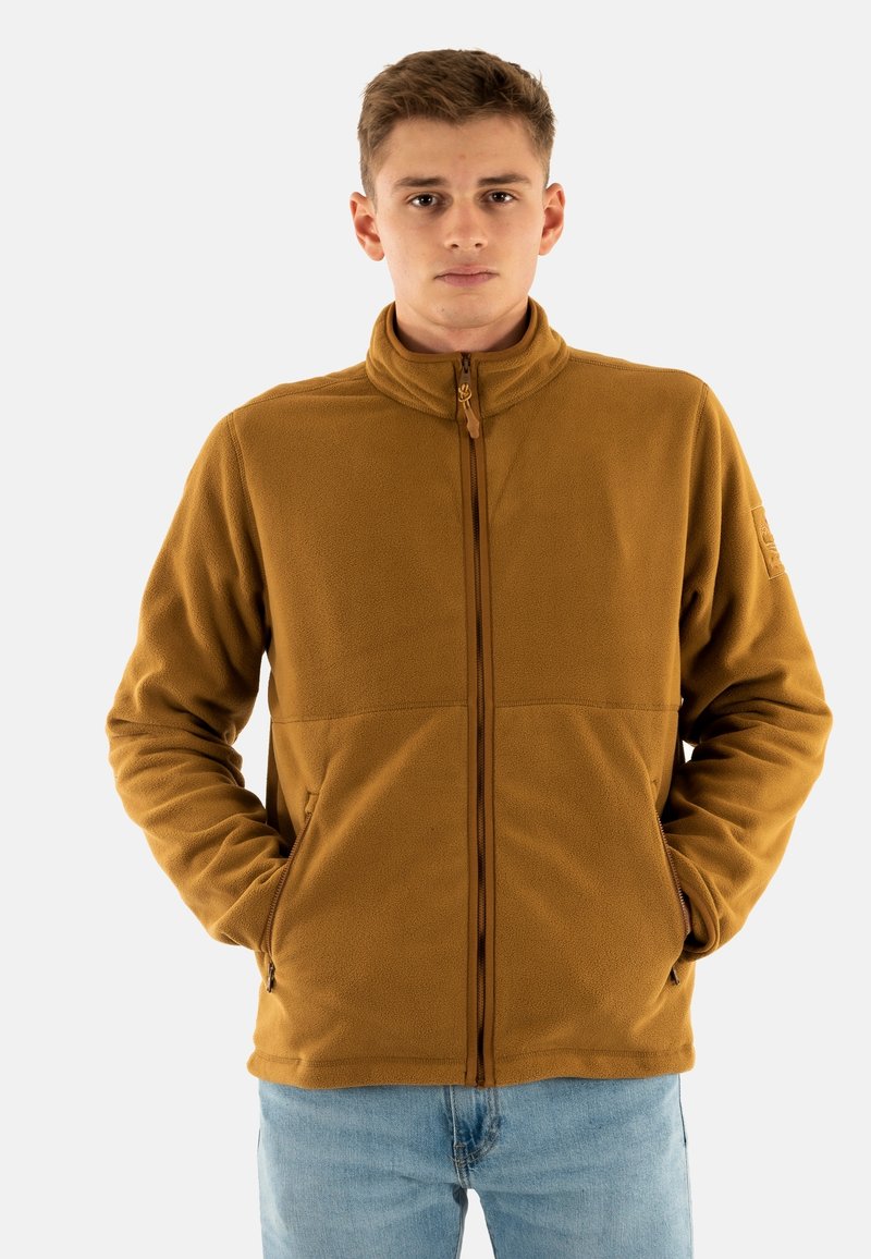 Chaqueta de forro polar en marrón cálido con un alto cuello, cremallera frontal y bolsillos laterales; presenta una textura suave y un diseño minimalista.