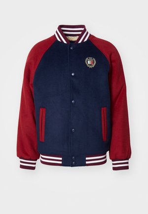 Veste universitaire bleu marine à manches rouges, avec col, poignets et bas rayés, boutons-pression, deux poches et un écusson sur la poitrine.