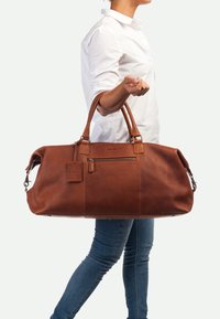 Bruine leren weekendtas met gestructureerd oppervlak, ritsvak en dubbele handgrepen. Inclusief een afneembare label en metalen hardware-accenten.