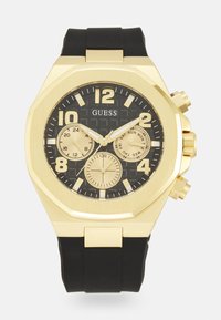 Reloj octogonal en tono dorado con correa de goma negra, cuenta con un dial negro texturizado, grandes números dorados y tres subdiales de cronógrafo.