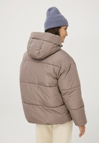 Giubbotto imbottito marrone chiaro con cappuccio, caratterizzato da sezioni trapuntate orizzontali. Abbinato a un berretto a costine azzurro chiaro.