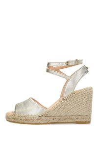 Sandalia de cuña con parte superior metálica plateada, punta abierta y correas cruzadas en los tobillos. Presenta una plataforma y un tacón envueltos en yute texturizado.