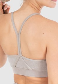 Sujetador deportivo gris claro con tirantes finos, diseño sin costuras y banda ribeteada. Presenta un estilo de espalda nadadora y una textura suave.