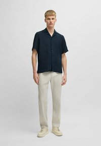 Korte mouwen, donkerblauwe button-up shirt met een ontspannen fit. Gecombineerd met lichtgekleurde broeken en beige sneakers, met een gladde textuur.