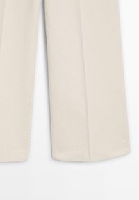Pantalon beige à jambes larges en tissu doux, présentant une texture lisse et des lignes épurées, avec un ourlet simple et sans éléments métalliques visibles.
