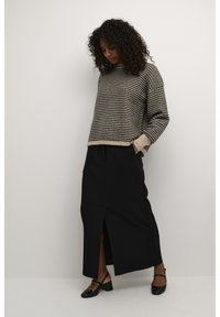 Jupe noire taille haute avec une fente à l'avant, assortie à un pull texturé rayé marron et crème. Des chaussures noires complètent la tenue.