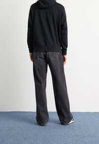 Svart hoodie med känguruficka, bärs med löst sittande, urtvättade svarta jeans. Outfiten fulländas med svartvita sneakers.