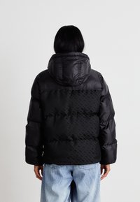 Mustat puffertakit, joissa on huppu, tarjoavat tikattua muotoilua ja hienovaraisia geometrisia kuvioita selässä. Valmistettu sileästä ja kiiltävästä materiaalista.