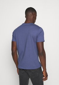 Krátký rukáv, námořnický modrý tričko vyrobené z měkké látky, s kulatým výstřihem a volným střihem. Zadní pohled ukazuje hladký povrch.