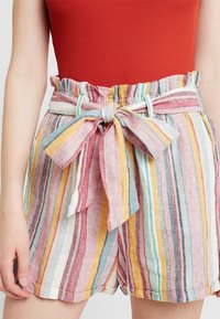 Pestré pruhované šortky s volánkovým pasem a tkanicemi. Vyrobené z lehkého materiálu, s růžovými, modrými, žlutými a bílými pruhy.