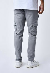 Pantaloni cargo grigi con molte tasche laterali, design affusolato, realizzati in tessuto leggero, abbinati a sneakers bianche.