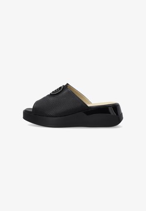 Sort slip-on sandal med perforeret overdel, åben tå, polstret sål og dekorativ rhinstenemblem på toppen.