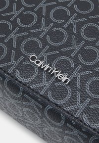 Geantă cosmetică texturată neagră, cu un model monogramă CK pe toată suprafața și un accent cu logo-ul "Calvin Klein" argintiu.