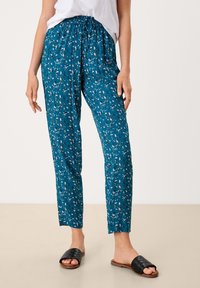 Teal bloemenprint broek met een elastische tailleband, taps toelopende pasvorm en lichtgewicht stof. Gepaard met zwarte gevlochten sandalen.