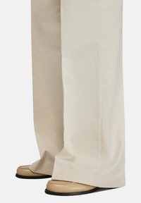 Pantaloni beige a gamba larga con una texture liscia, abbinati a mocassini color cammello con design cucito e suole in gomma nere.