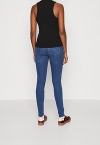 Jeans de denim azul ajustados con un ligero desgaste, bolsillos traseros y un diseño ceñido, combinados con una camiseta sin mangas negra y zapatillas burdeos.