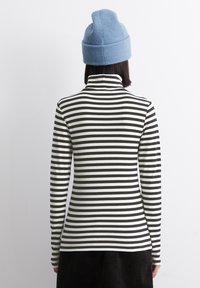 Juoda ir balta juostuota turtlenecko palaidinė su ilgomis rankovėmis, turinti minkštą, banguotą tekstūrą. Pasirinkta su mėlyna megzta kepure.
