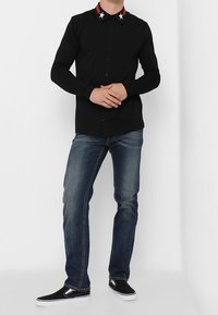 Camisa negra de manga larga con cuello estampado de estrellas, combinada con jeans azules y zapatos negros sin cordones. Tejido suave, diseño ajustado.