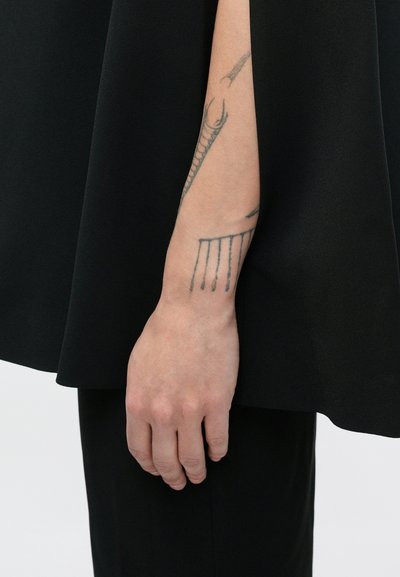 Parem ettevars ja käsi, millel on lineaarse musta tindiga tätoveeringud, musta riietusega ja hele taust.